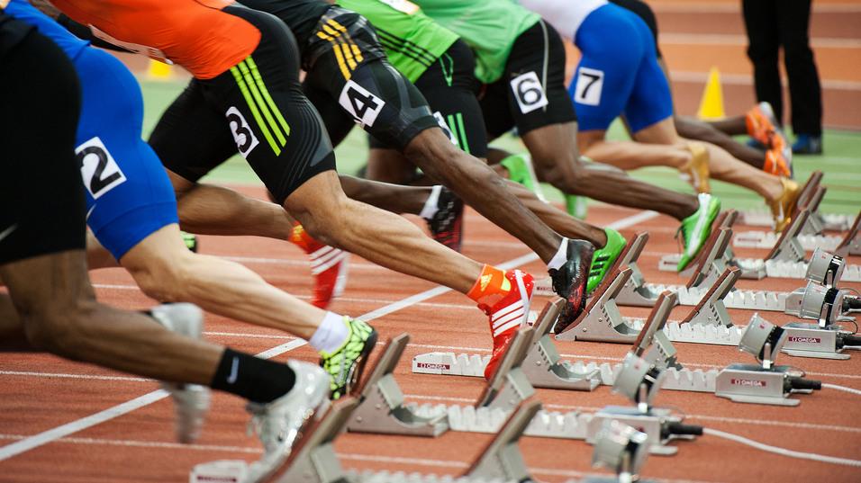 Start einer Sprintveranstaltung mit mehreren Athleten in Blockstartposition auf einer Laufbahn.